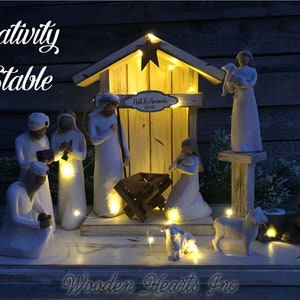 May include: A white wooden nativity stable with a white star on the roof. The stable is lit with white fairy lights and has a sign that reads "Neil & Amanda 2018". There are white figurines of Mary, Joseph, baby Jesus, and the three wise men. There are also two white sheep and a brown donkey.