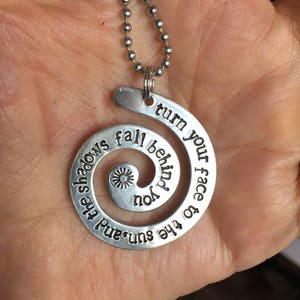 Può includere: Collana d'argento con un ciondolo a spirale che recita "Volgi il tuo viso al sole e le ombre cadranno dietro di te".