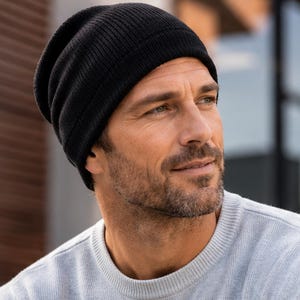 May include: A solid black knit beanie cap featuring a ribbed texture and a folded cuff design. The hat is constructed from a soft, flexible material that fits snugly around the head, providing a classic look with a simple, clean aesthetic.
