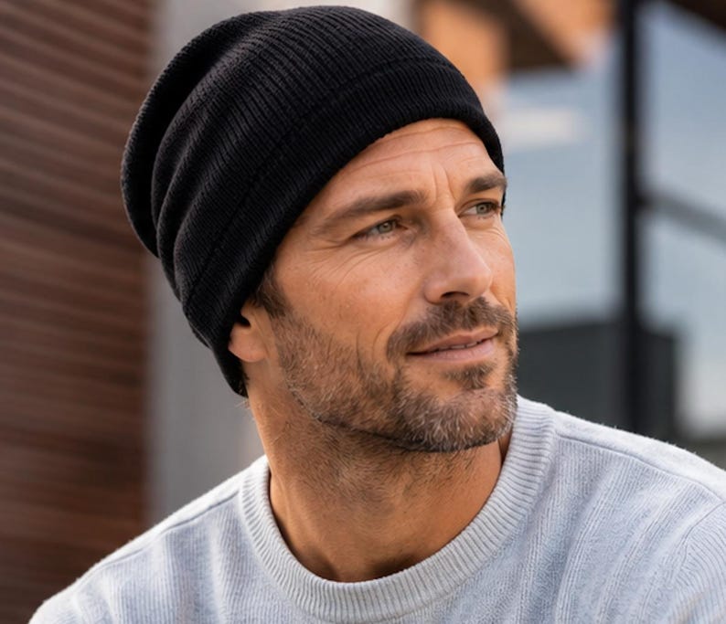 May include: A solid black knit beanie cap featuring a ribbed texture and a folded cuff design. The hat is constructed from a soft, flexible material that fits snugly around the head, providing a classic look with a simple, clean aesthetic.