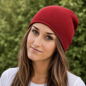 May include: A solid deep red beanie hat featuring a fine ribbed knit texture. The hat has a simple rounded crown and a clean, finished edge that sits comfortably around the head, providing a consistent color and uniform knit pattern throughout.