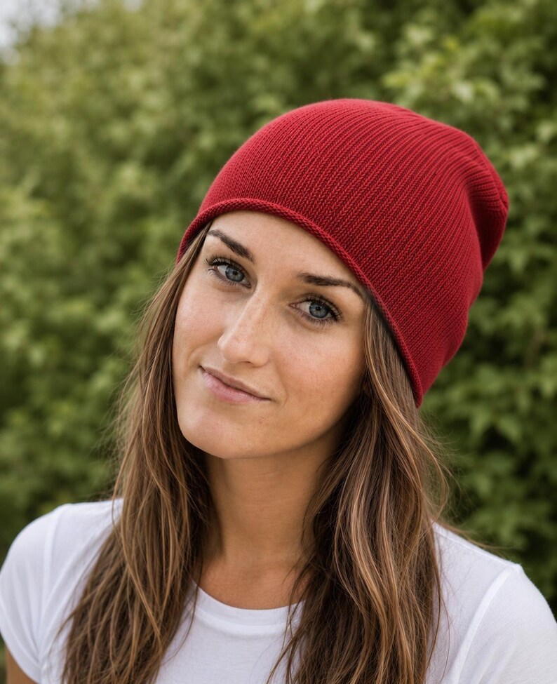 May include: A solid deep red beanie hat featuring a fine ribbed knit texture. The hat has a simple rounded crown and a clean, finished edge that sits comfortably around the head, providing a consistent color and uniform knit pattern throughout.