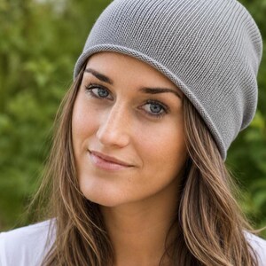 May include: A light gray beanie hat featuring a fine ribbed knit texture and a simple rolled edge hem. The hat is constructed from a soft, lightweight material and sits comfortably on the head with a slightly slouchy fit at the crown.