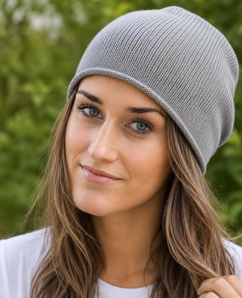 May include: A light gray beanie hat featuring a fine ribbed knit texture and a simple rolled edge hem. The hat is constructed from a soft, lightweight material and sits comfortably on the head with a slightly slouchy fit at the crown.