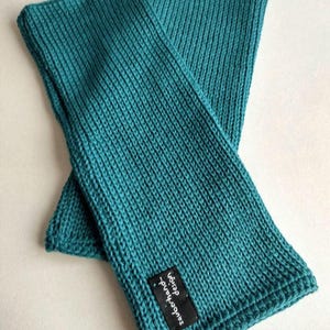May include: A pair of teal blue knitted arm warmers with a black label that says "Handmade - Etsy".