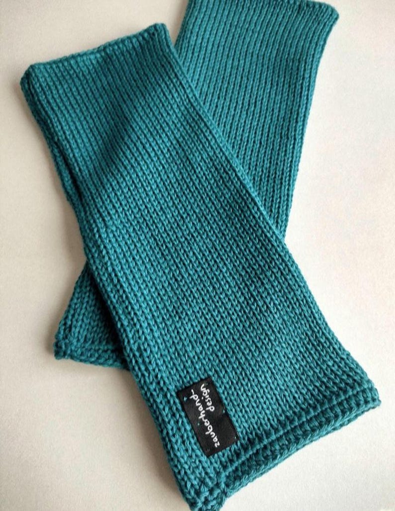 May include: A pair of teal blue knitted arm warmers with a black label that says "Handmade - Etsy".