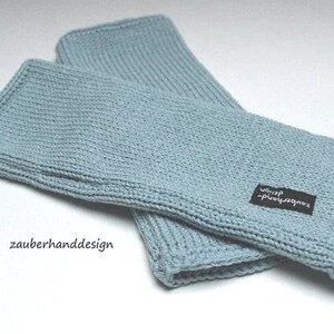 May include: A pair of light blue knitted wrist warmers with a black label that says "zauberhanddesign -  wolle".