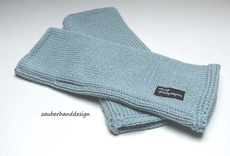 May include: A pair of light blue knitted wrist warmers with a black label that says "zauberhanddesign -  wolle".