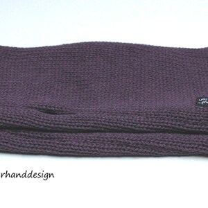 May include: Purple knitted fingerless gloves with a black label that says "zauberhanddesign".