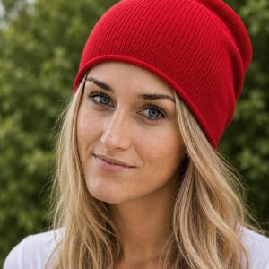 May include: A vibrant red beanie hat featuring a fine-knit texture and a simple, rounded crown design. The cap is constructed with a smooth, consistent stitch pattern throughout, providing a clean look that sits comfortably on the head.