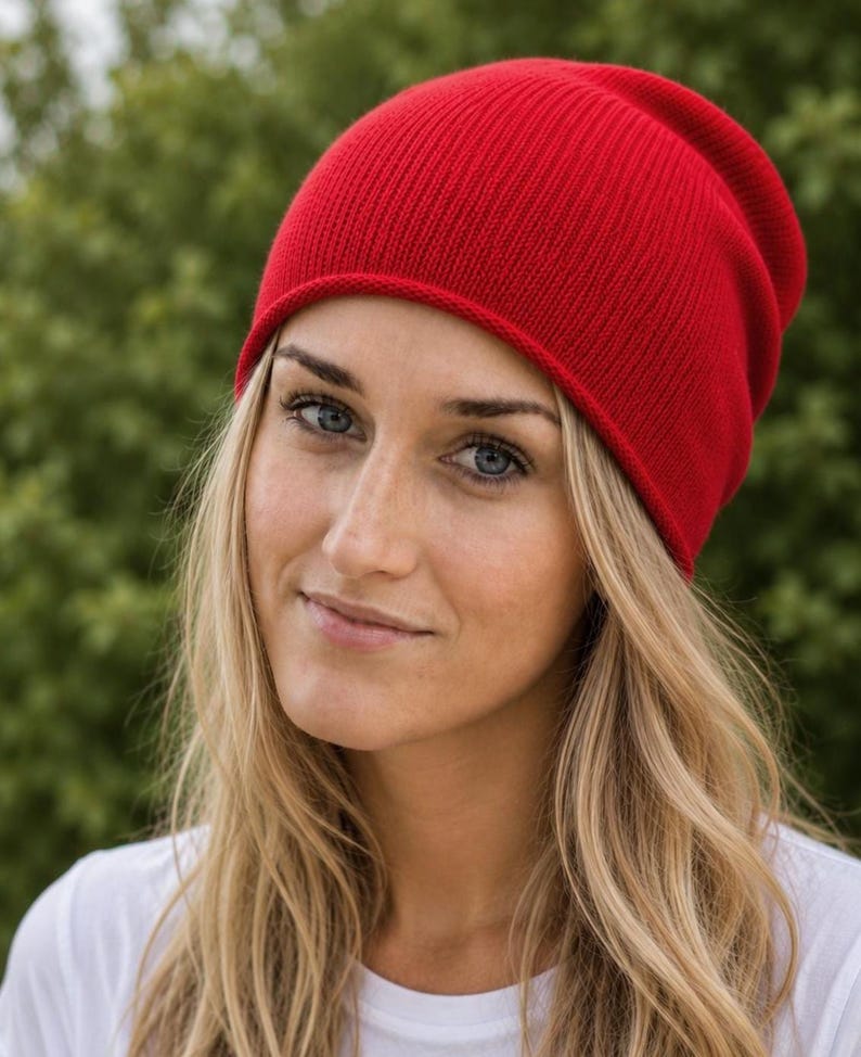 May include: A vibrant red beanie hat featuring a fine-knit texture and a simple, rounded crown design. The cap is constructed with a smooth, consistent stitch pattern throughout, providing a clean look that sits comfortably on the head.