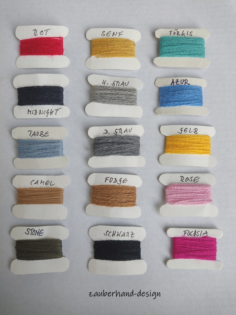 May include: Fifteen spools of yarn in various colors including red, mustard, turquoise, midnight blue, light gray, azure, taupe, dark gray, yellow, camel, fudge, rose, stone, black, and fuchsia. Each spool has a handwritten label above it.