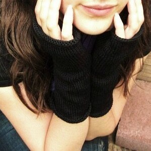 May include: A pair of black knit fingerless gloves with a ribbed texture.