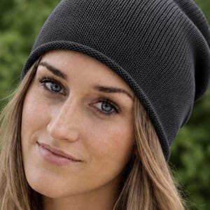 May include: A dark charcoal gray knit beanie with a simple, rounded silhouette and a subtle rolled edge. The hat is constructed from a fine, uniform ribbed knit fabric that provides a smooth texture and a consistent, deep gray color throughout.
