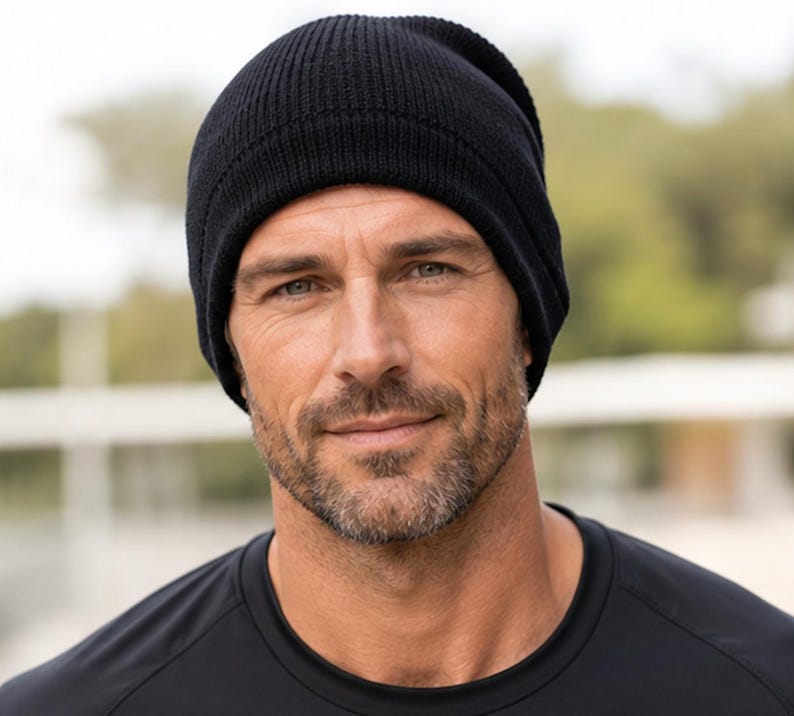 May include: A solid black beanie made of a ribbed knit fabric. The hat features a classic rounded crown design with a folded cuff at the base, providing a snug fit around the head. The material has a consistent dark black color throughout the entire piece.