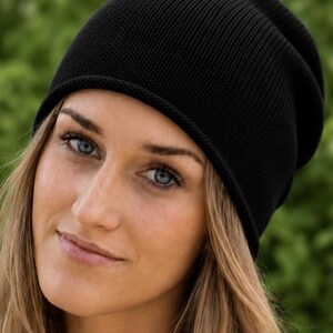 May include: A solid black beanie with a fine knit texture and a simple rolled edge. The hat features a classic slouchy silhouette that sits comfortably on the head, providing a clean and uniform appearance in a deep, dark black color.