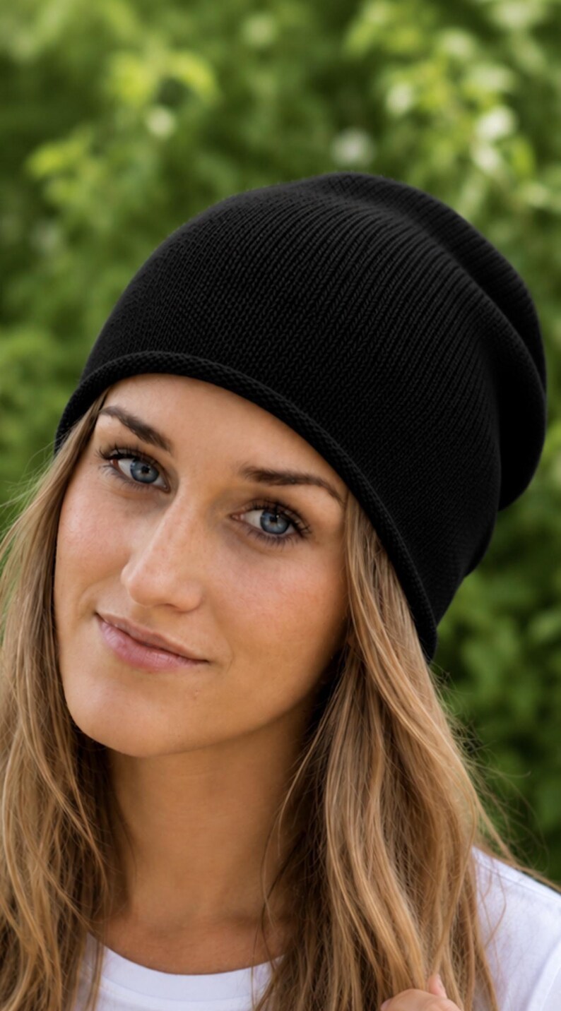 May include: A solid black beanie with a fine knit texture and a simple rolled edge. The hat features a classic slouchy silhouette that sits comfortably on the head, providing a clean and uniform appearance in a deep, dark black color.