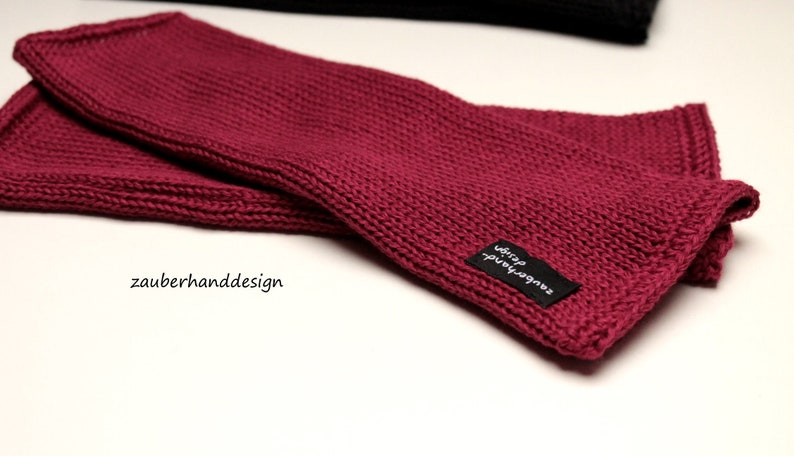 May include: A pair of burgundy knitted wrist warmers with a black label that reads "zauberhand design".