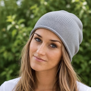 May include: A light gray beanie hat made of a fine-knit fabric with a simple, rounded crown and a soft, rolled edge. The hat features a consistent, smooth texture throughout, providing a clean and understated look for everyday headwear.