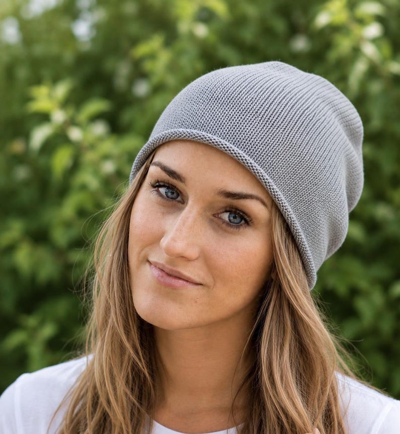 May include: A light gray beanie hat made of a fine-knit fabric with a simple, rounded crown and a soft, rolled edge. The hat features a consistent, smooth texture throughout, providing a clean and understated look for everyday headwear.