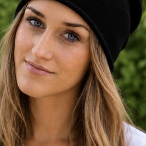 May include: A solid black knit beanie with a simple, rounded crown and a clean, finished edge. The hat is constructed from a fine-gauge knit fabric, providing a smooth, uniform texture that fits snugly around the head in a classic, versatile style.