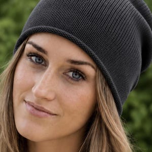 May include: A dark charcoal gray beanie with a fine knit texture and a slightly slouchy fit. The hat features a simple, clean design with a rolled edge at the bottom, providing a smooth and consistent appearance across the entire surface of the cap.