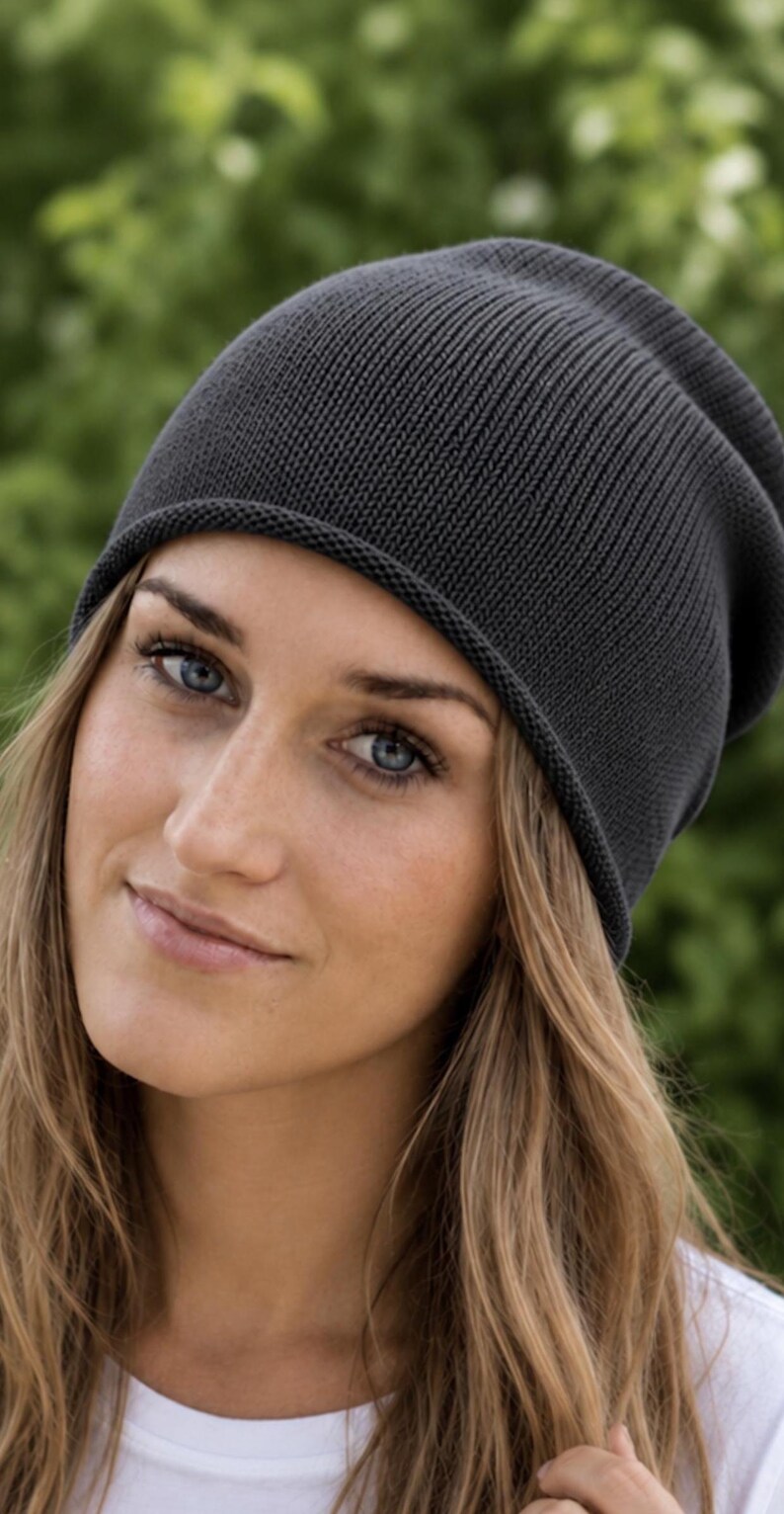 May include: A dark charcoal gray beanie with a fine knit texture and a slightly slouchy fit. The hat features a simple, clean design with a rolled edge at the bottom, providing a smooth and consistent appearance across the entire surface of the cap.