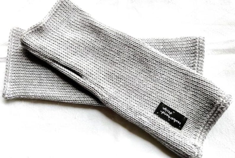 May include: A pair of gray knitted fingerless gloves with a black label that reads "handmade with love".