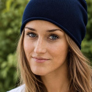 May include: A solid dark navy blue beanie hat featuring a fine-knit texture and a simple rolled edge design. The hat is constructed from a soft, flexible fabric that fits snugly around the head, providing a clean and uniform appearance throughout.
