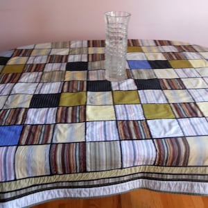 Peut inclure: Une nappe ovale &agrave; motifs avec un design patchwork aux couleurs vari&eacute;es, dont le bleu, le noir et le jaune. Un vase en verre transparent textur&eacute; est pos&eacute; sur la table. La nappe pr&eacute;sente un motif &agrave; rayures.
