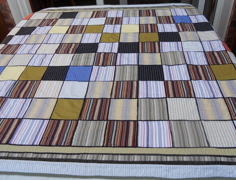 Peut inclure: Une courtepointe patchwork avec un motif quadrill&eacute;, compos&eacute;e de carr&eacute;s de diff&eacute;rents tissus. Les carr&eacute;s comprennent des tissus ray&eacute;s et unis dans des couleurs comme le bleu, le noir, le jaune et le marron. La courtepointe a une bordure ray&eacute;e.