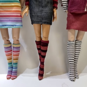 May include: Three pairs of doll legs with different striped knee-high socks. The socks are rainbow, red and black, and white and black.