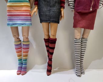 May include: Three pairs of doll legs with different striped knee-high socks. The socks are rainbow, red and black, and white and black.