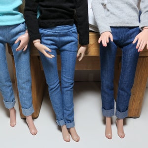 May include: Three pairs of blue jeans with rolled up cuffs. The jeans are on the legs of three dolls.