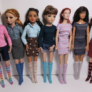 May include: Eight fashion dolls with different hairstyles and outfits. The dolls are wearing a variety of clothing, including skirts, dresses, shorts, and shirts. They are all wearing knee-high socks in different colors and patterns.