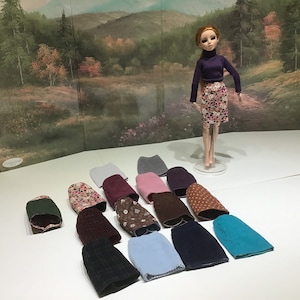 May include: A collection of 14 different fabric skirts in various colors and patterns, including floral, polka dot, and solid colors. The skirts are arranged in a semi-circle on a white surface.