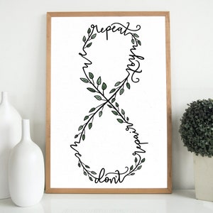 Peut inclure: Une impression encadrée avec un symbole d'infini noir fait de branches feuillues. Les mots "ne répète pas hier" sont écrits autour du symbole.