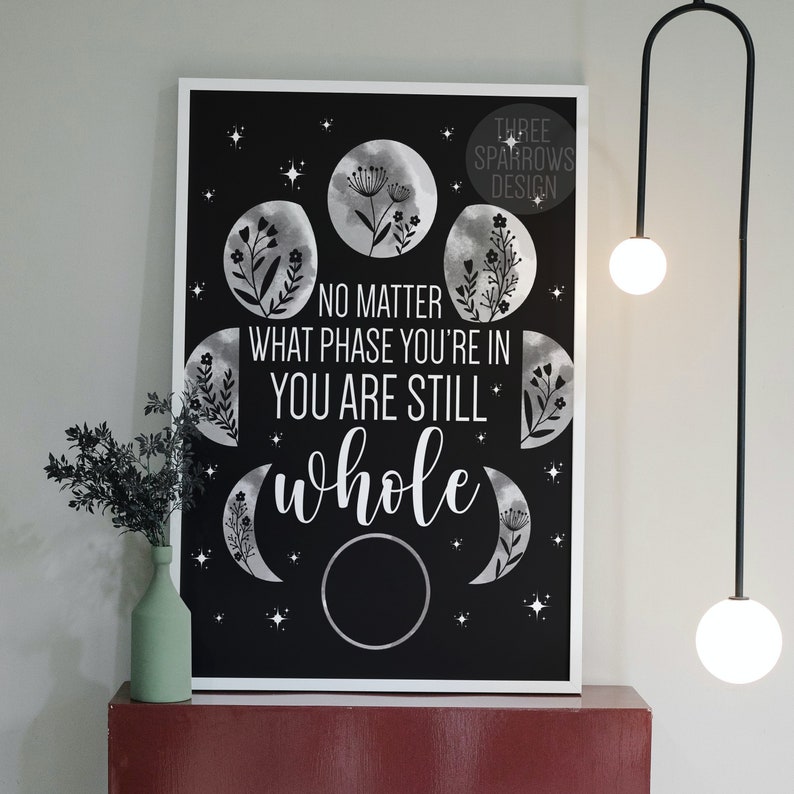 May include: Black and white print with a quote that reads "No matter what phase you're in you are still whole". The quote is surrounded by moon phases with floral designs.