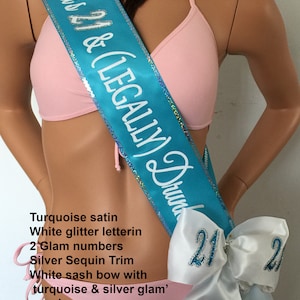 K&ouml;nnte beinhalten: T&uuml;rkiser Satin-Sch&auml;rpe mit wei&szlig;er Glitzer-Beschriftung "Olivia's 21 & (LEGALLY) Drunk". Die Sch&auml;rpe hat einen silbernen Paillettenbesatz und eine wei&szlig;e Schleife mit t&uuml;rkisfarbenen und silbernen Glitzerzahlen.