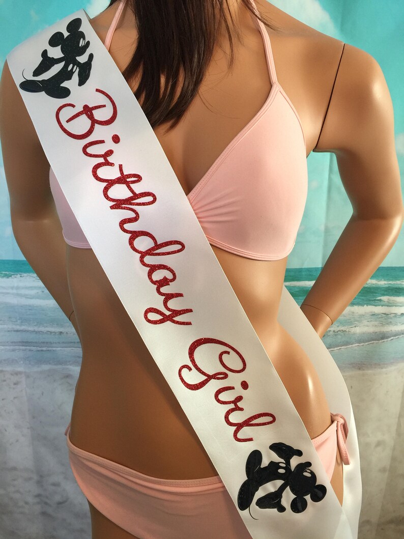 May include: White satin sash with red glitter text that reads "Birthday Girl". The sash has a black and white Mickey Mouse silhouette on each end.