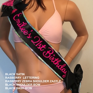 K&ouml;nnte beinhalten: Ein schwarzes Satinschleife mit silbernem Glitzerbesatz und rosa Schriftzug "Emilee's 21st Birthday".