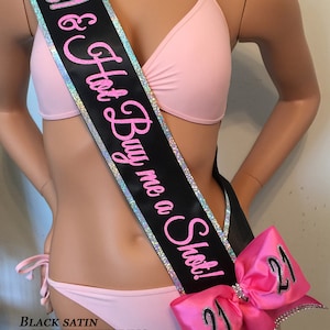 Puede incluir: Sash de sat&eacute;n negro con ribete plateado y letras rosa intenso que dicen "21 & Hot Buy me a Shot!"  El sash tiene un gran lazo rosa con dos n&uacute;meros "21" plateados.