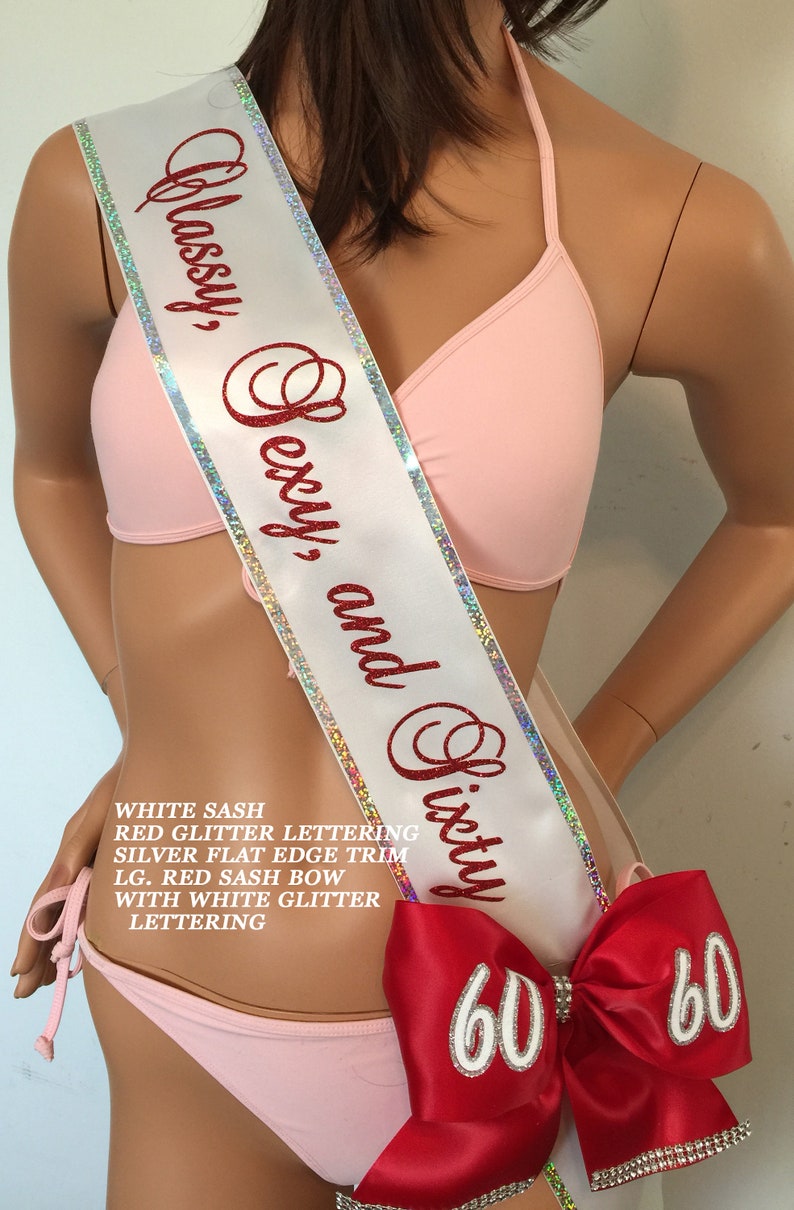 Puede incluir: Sash de sat&eacute;n blanco con letras de purpurina roja que dicen "Classy, Sexy, and Sixty". El sash tiene un ribete plano plateado y un gran lazo de sat&eacute;n rojo con letras de purpurina blanca que dicen "60".