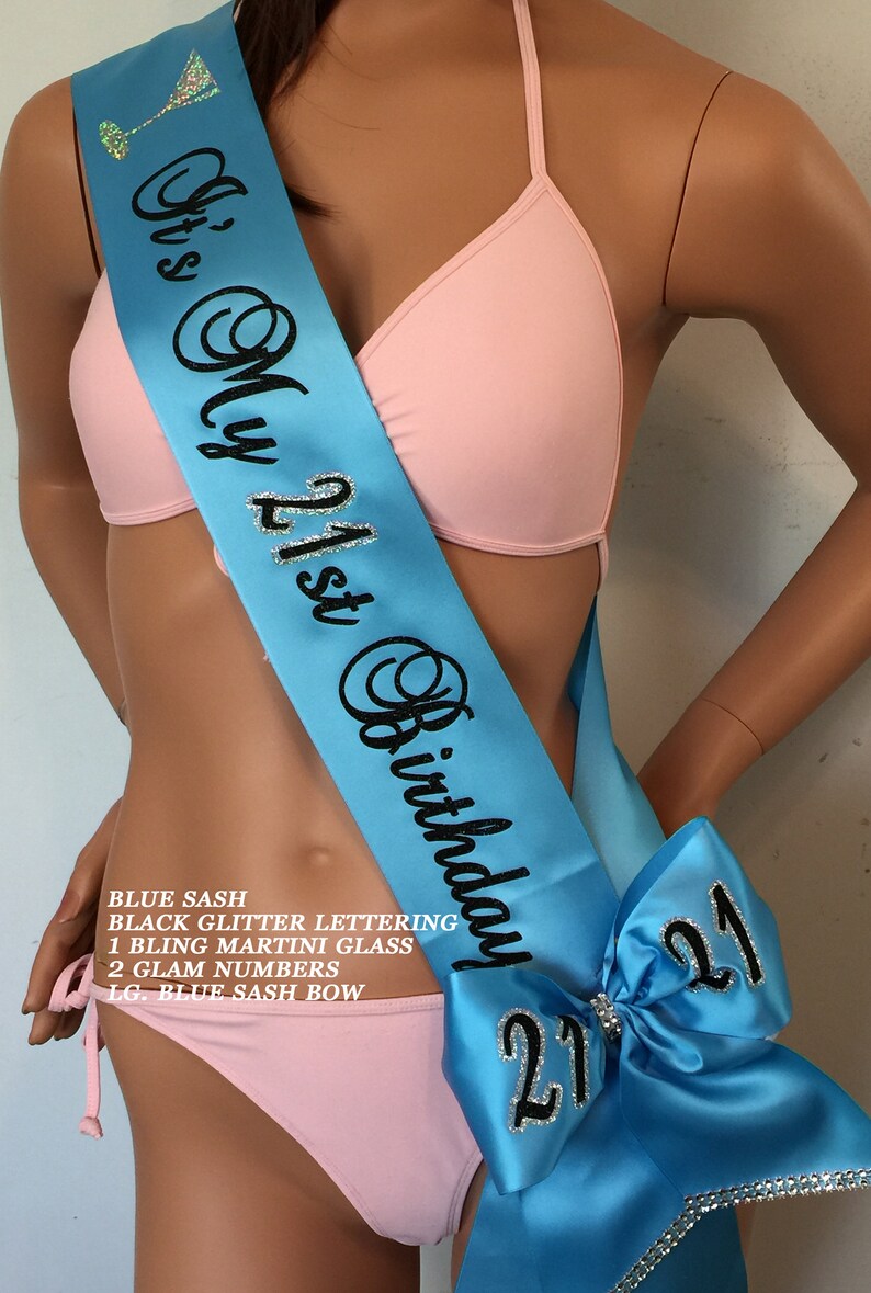 K&ouml;nnte beinhalten: Blauer Satin-Sch&auml;rpe mit schwarzer Glitzer-Beschriftung "It's My 21st Birthday". Die Sch&auml;rpe hat eine gro&szlig;e blaue Schleife mit einer silbernen Glitzer-&bdquo;21&ldquo; darauf.
