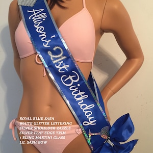 May include: A royal blue satin sash with silver glitter lettering that reads "Allison's 21st Birthday". The sash has a silver shoulder trim, a silver flat edge trim, a bling martini glass charm, and a large blue satin bow.