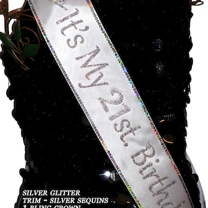 May include: White satin sash with silver glitter trim and silver sequins. The sash has the text "It's My 21st. Birthday!" in silver rhinestones.