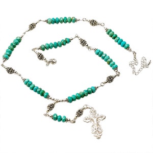 May include: A turquoise and silver necklace with a cross pendant. The necklace is made of turquoise beads and silver chain links. The cross pendant is silver and has a detailed design.