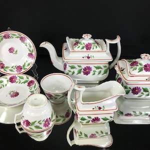 May include: A vintage tea set with a floral design. The set includes a teapot, creamer, sugar bowl, and two teacups and saucers. The floral design features pink flowers and green leaves on a white background.