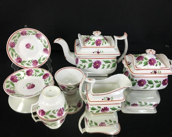 May include: A vintage tea set with a floral design. The set includes a teapot, creamer, sugar bowl, and two teacups and saucers. The floral design features pink flowers and green leaves on a white background.