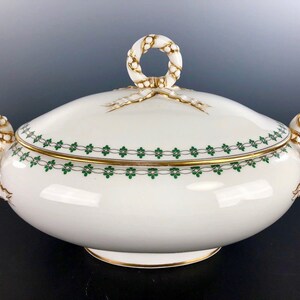 May include: White porcelain serving dish with lid, featuring green floral and gold trim. The dish has a loop handle on the lid and two side handles. The design includes gold accents and a decorative green floral border.